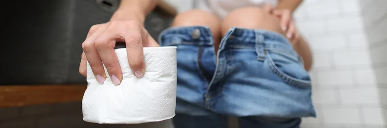 Osoba sedící na záchodě s toaletním papírem v ruce.