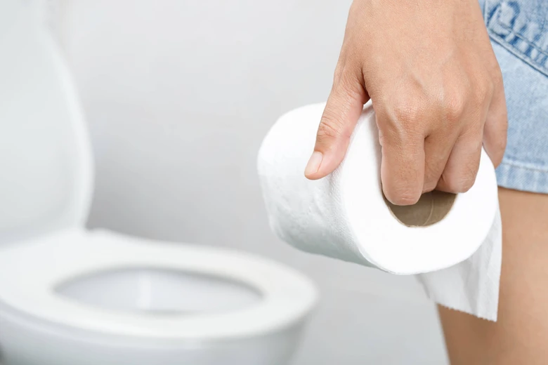 Ruka drží toaletní papír před záchodem v koupelně.
