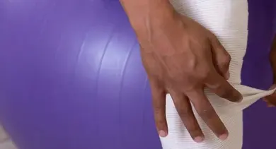 Ruční obalování fialového cvičacího míče bílou páskou.