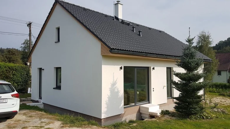 Moderní bílý bungalov s tmavou střechou a velkými okny.