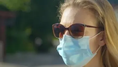 Žena venku v modré roušce a slunečních brýlích.