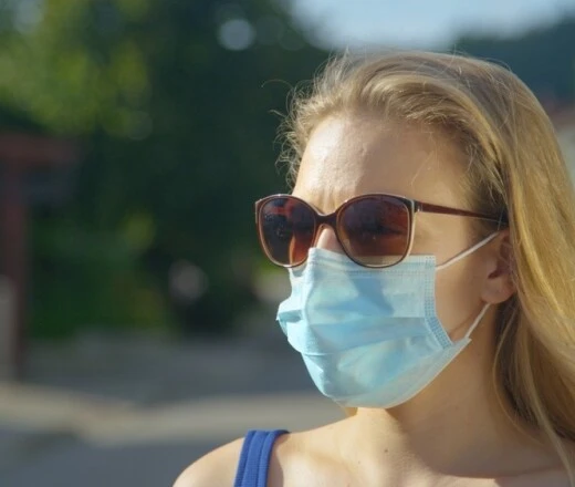 Žena venku v modré roušce a slunečních brýlích.