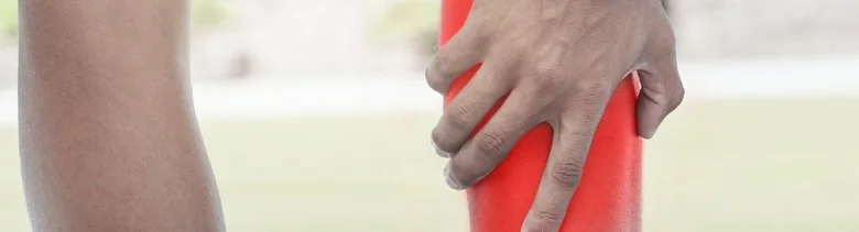 Ruka drží červený válec u lýtkového svalu
