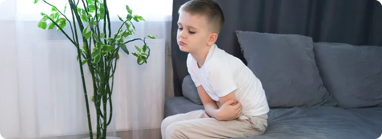 Smutný chlapec sedí na gauči, možná má průjem.