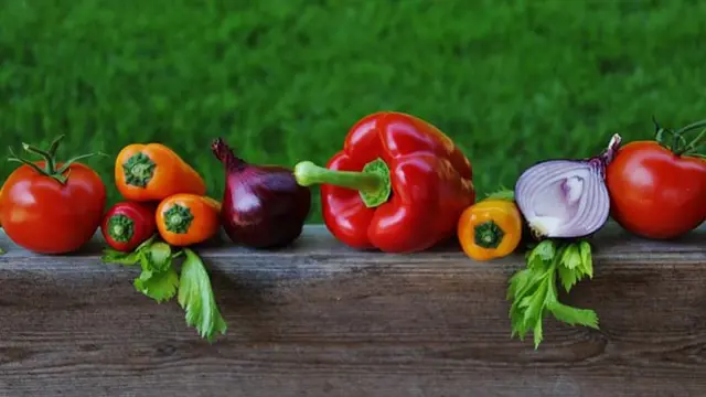 Čerstvá rajčata, papriky, cibule a petržel na dřevěném prknu.