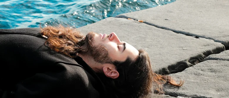 Muž leží u vody v relaxační poloze pro meditaci.