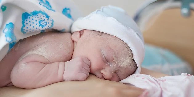 Spící novorozené dítě v bílé čepici na rukou dospělého.