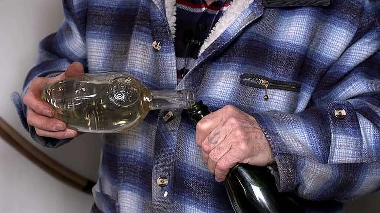 Muž nalévá tekutinu z jednoho lahví do druhé.