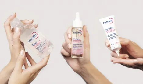 Ruce drží produkty Bioderma pro péči o pleť s růžovkou.
