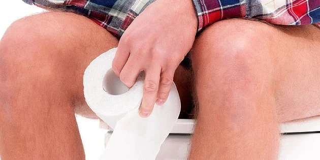 Muž sedí na záchodě s toaletním papírem v ruce.