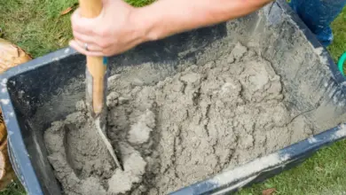 Člověk míchá beton lopatou v plastovém voze na trávě.