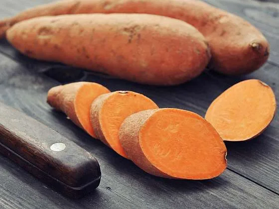 Celé i nakrájené batáty s nožem na dřevěném povrchu.