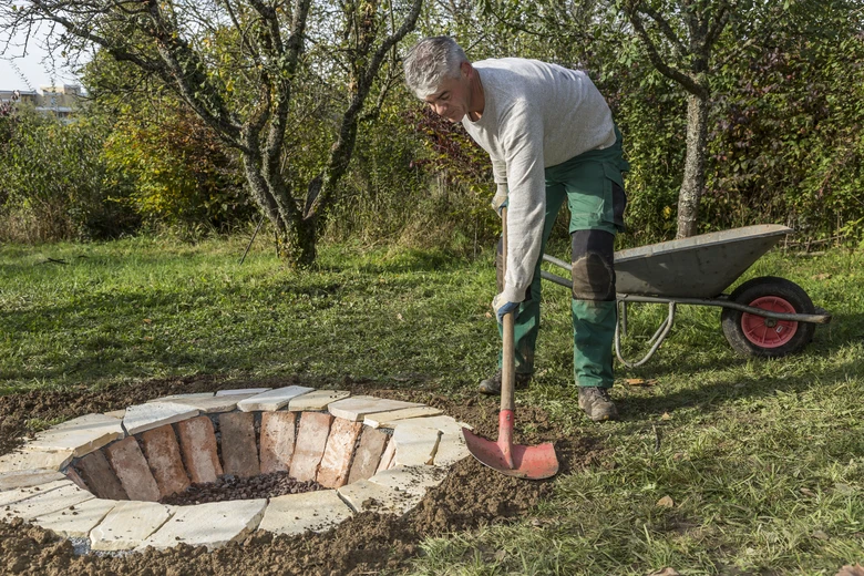 Muž staví kruhové ohniště z cihel v zahradě.