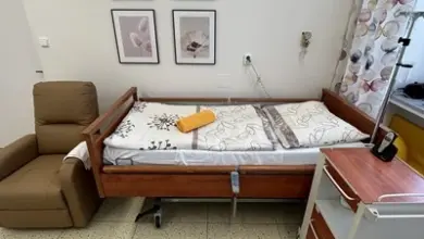 Fotografie čisté porodní místnosti s lůžkem a židlí.