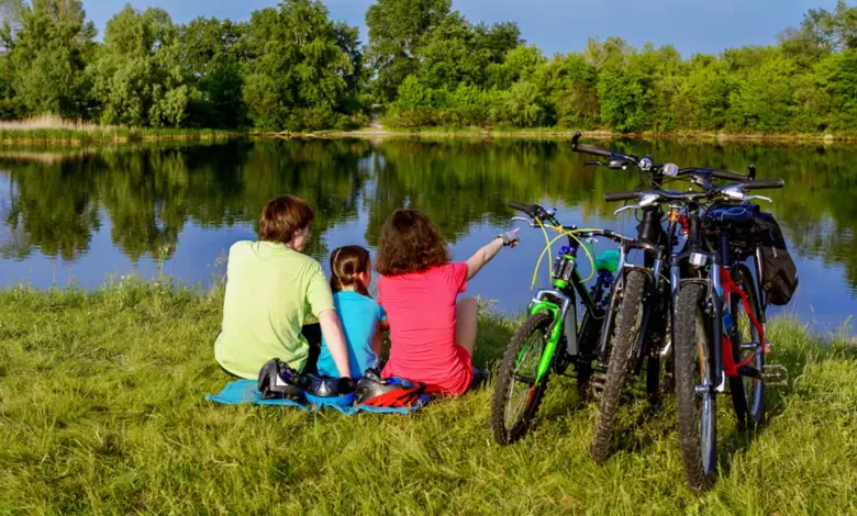 Rodina s dětmi sedí u jezera se svými bicykly.