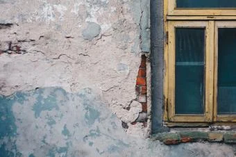 Zvětralá omítka na zdi u okna v rodinném domě.