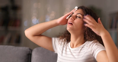 Žena sedí na gauči a drží si hlavu kvůli bolesti.